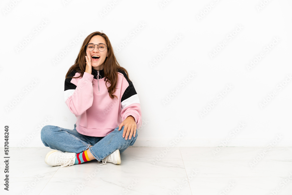 Young caucasian woman sitting on the floor isolated on white background shouting with mouth wide open Young caucasian woman sitting on the floor isolated on white background shouting with mouth wide open