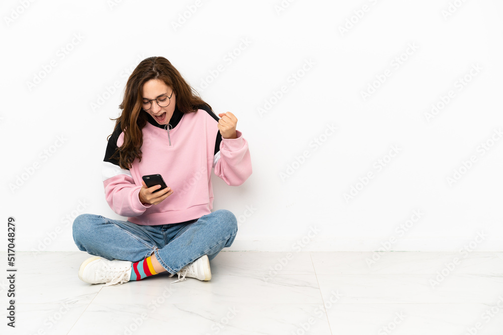 Young caucasian woman sitting on the floor isolated on white background surprised and sending a message Young caucasian woman sitting on the floor isolated on white background surprised and sending a message