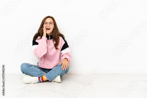 Young caucasian woman sitting on the floor isolated on white background shouting with mouth wide open