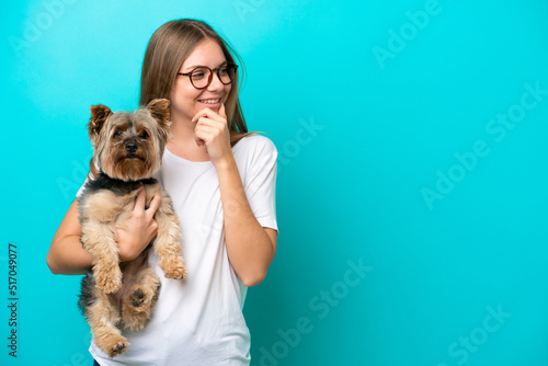 Young Lithuanian woman holding a dog isolated on blue background thinking an idea and looking side