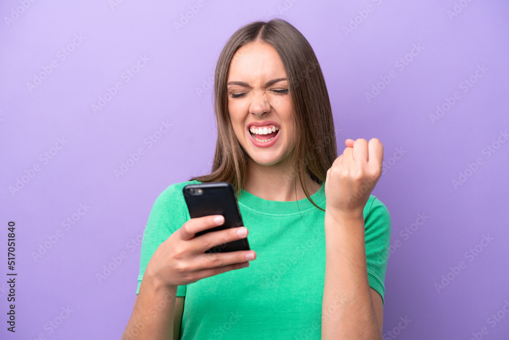 Young caucasian woman isolated on purple background with phone in victory position