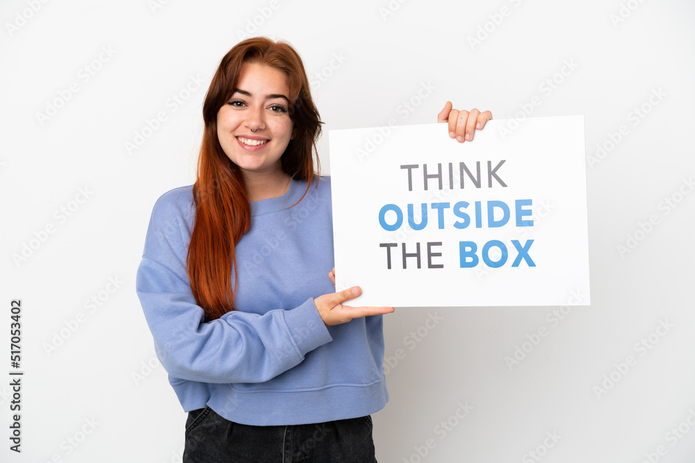 Young redhead woman isolated on white background holding a placard with text Think Outside The Box with happy expression Young redhead woman isolated on white background holding a placard with text Think Outside The Box with happy expression