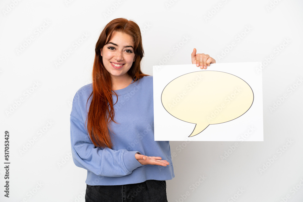 Young redhead woman isolated on white background holding a placard with speech bubble icon and pointing it Young redhead woman isolated on white background holding a placard with speech bubble icon and pointing it