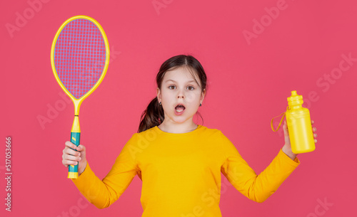 amazed kid hold tennis racket and water bottle on pink background