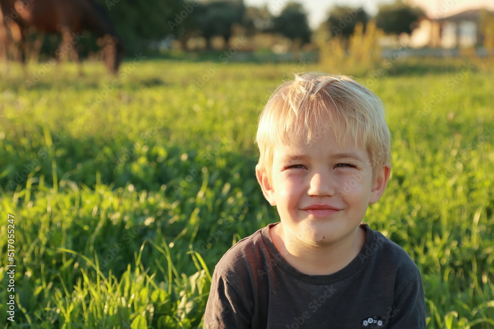 A smiling 4-year-old little blond toddler boy is sitting in green yellow sunny autumn meadow and smiling A smiling 4-year-old little blond toddler boy is sitting in green yellow sunny autumn meadow and smiling