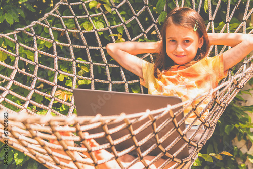 Huppy young girl working remotely with laptop outdoors in a hammock. Summer holiday and remotely work concept. Horizontal image. photo