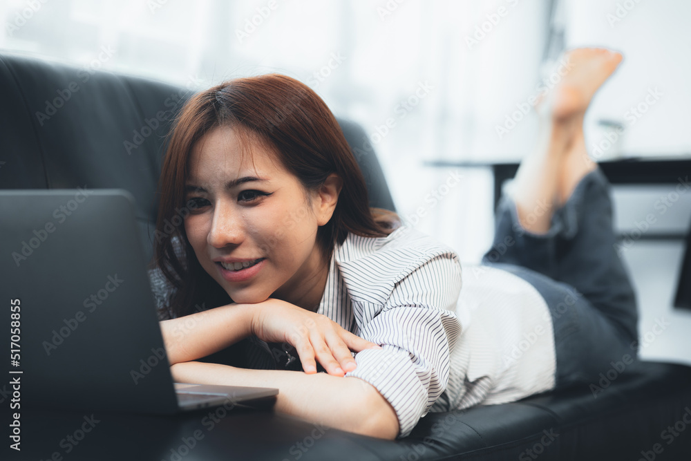 Asian woman lying on the sofa playing laptop on the sofa, she is taking a weekend break after a hard day's work. Holiday relaxation ideas. Asian woman lying on the sofa playing laptop on the sofa, she is taking a weekend break after a hard day's work. Holiday relaxation ideas.