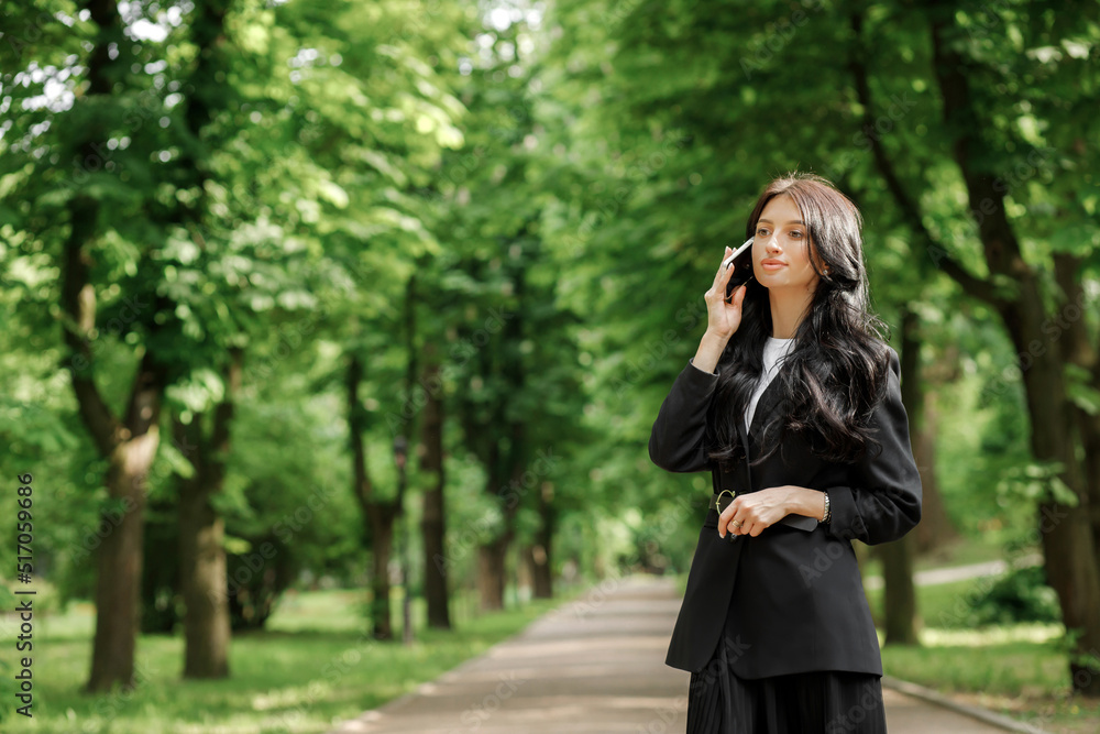 Business woman use cellphone outdoors. Beautiful focused young girl in a formal suit in the park. Mobile network, communication.