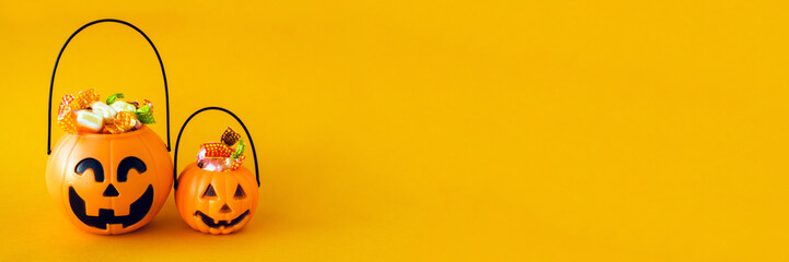 trick or treat for halloween. Pumpkin bucket with sweets and spiders on an orange background. Sweets for kids for Halloween. Copyspace. Web banner