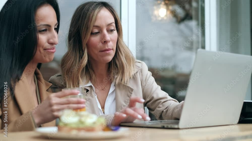 Video of two happy friends sharing a brunch together while working with laptop in the eco coffee shop terrace. Video of two happy friends sharing a brunch together while working with laptop in the eco coffee shop terrace.
