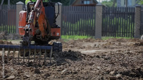 A mini excavator with a rake loosens the ground. landscape preparation