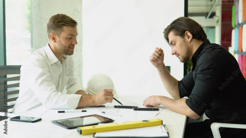 Two businessman engineers working in bright clean office. Discussing the construction project, plan, drawing, scheme Two businessman engineers working in bright clean office. Discussing the construction project, plan, drawing, scheme