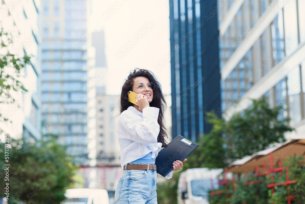 Young business woman walking across the road with tablet among the skyscrapers and speaks on the phone. Young business woman walking across the road with tablet among the skyscrapers and speaks on the phone.