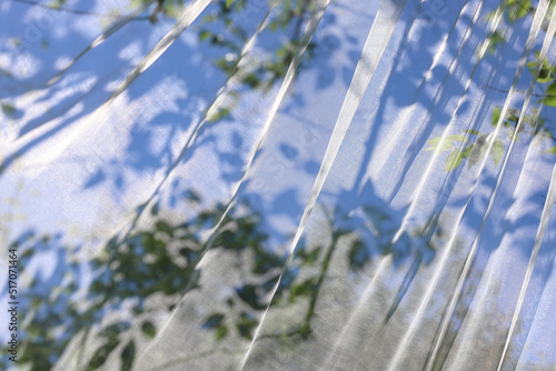 Wavy surface of a chiffon fabric with green and blue floral shadows as a background