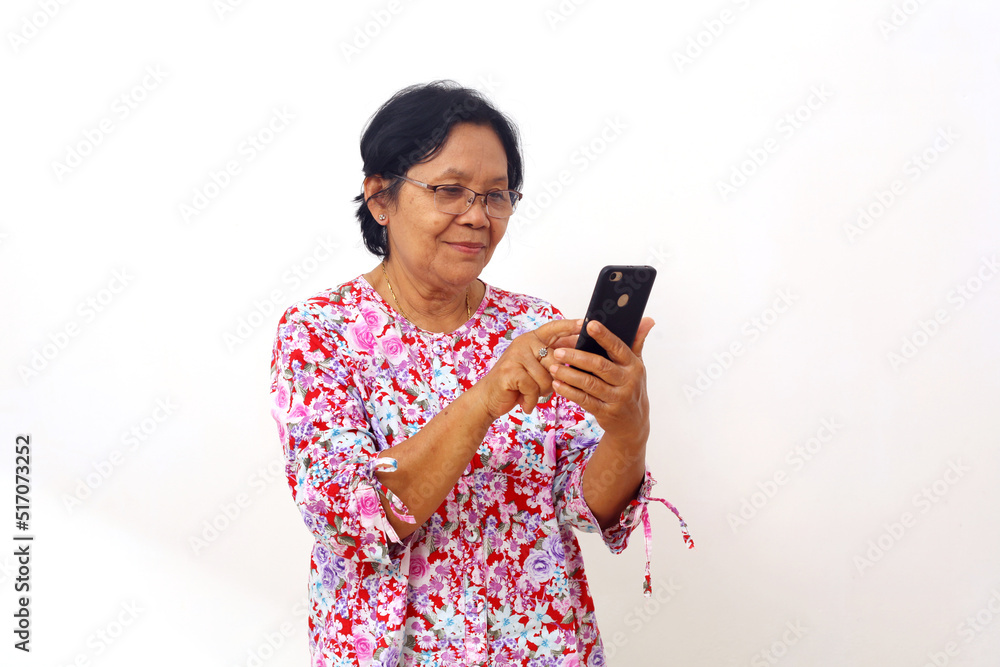 Happy asian elderly woman standing while holding and operating her cellular phone. Isolated on white Happy asian elderly woman standing while holding and operating her cellular phone. Isolated on white