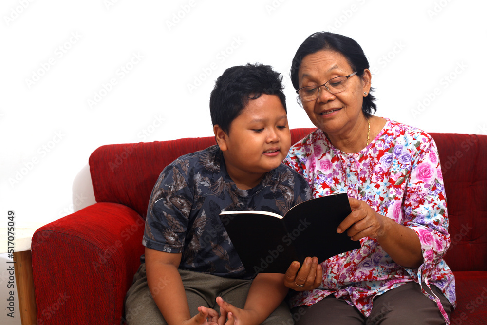 Obraz premium Front view of an Asian grandmother and her grandson reading a story book in living room at home