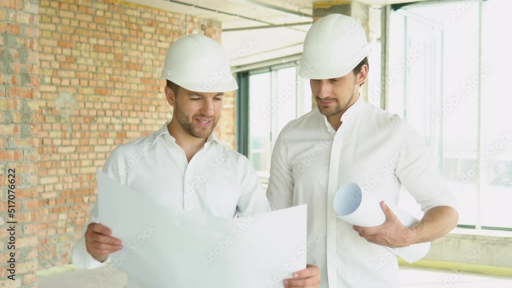 Two men in helmet look at the plan of the building Two men in helmet look at the plan of the building