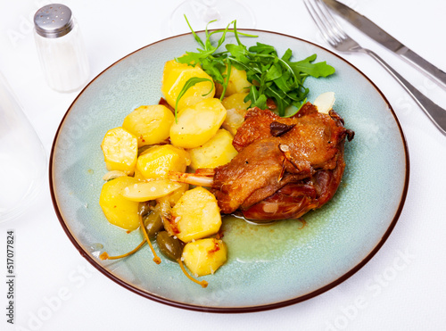 Just cooked portion of duck confit with fried poatoes served on table with serving pieces. photo