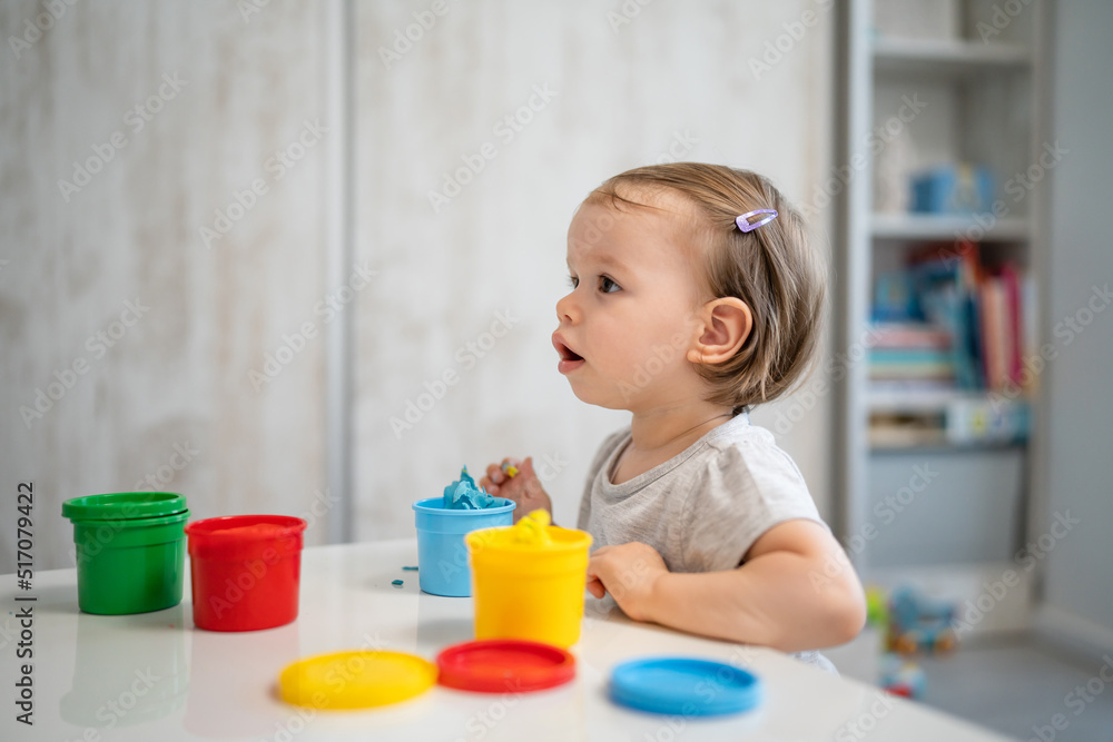 One girl small caucasian toddler child playing with colorful plasticine on the table at home alone childhood and growing up concept copy space side view One girl small caucasian toddler child playing with colorful plasticine on the table at home alone childhood and growing up concept copy space side view