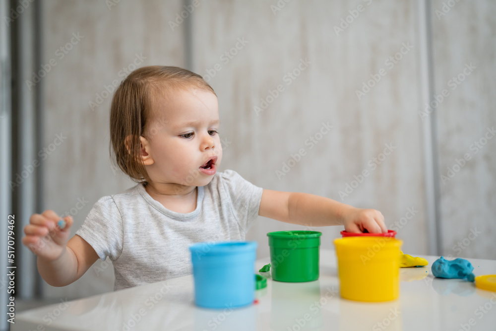 One girl small caucasian toddler child playing with colorful plasticine on the table at home alone childhood and growing up development concept copy space One girl small caucasian toddler child playing with colorful plasticine on the table at home alone childhood and growing up development concept copy space