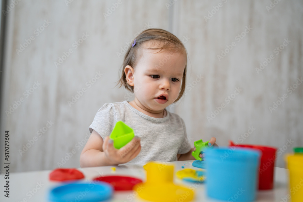 One girl small caucasian toddler child playing with colorful plasticine on the table at home alone childhood and growing up development concept copy space One girl small caucasian toddler child playing with colorful plasticine on the table at home alone childhood and growing up development concept copy space