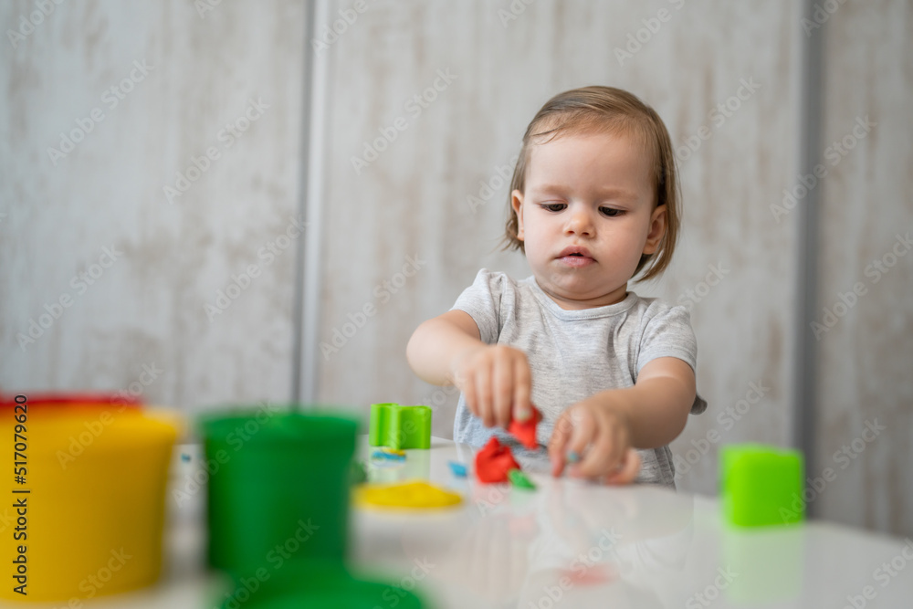 One girl small caucasian toddler child playing with colorful plasticine on the table at home alone childhood and growing up development concept copy space One girl small caucasian toddler child playing with colorful plasticine on the table at home alone childhood and growing up development concept copy space