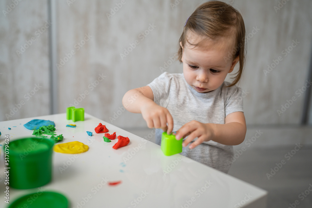 One girl small caucasian toddler child playing with colorful plasticine on the table at home alone childhood and growing up development concept copy space One girl small caucasian toddler child playing with colorful plasticine on the table at home alone childhood and growing up development concept copy space
