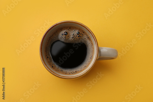 Cup of delicious black coffee on yellow background, top view photo