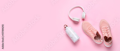 Sports shoes with headphones and bottle of water on pink background with space for text