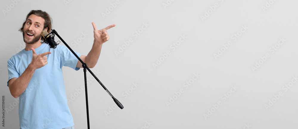 Handsome young man singing in microphone and pointing at something on light background with space for text Handsome young man singing in microphone and pointing at something on light background with space for text