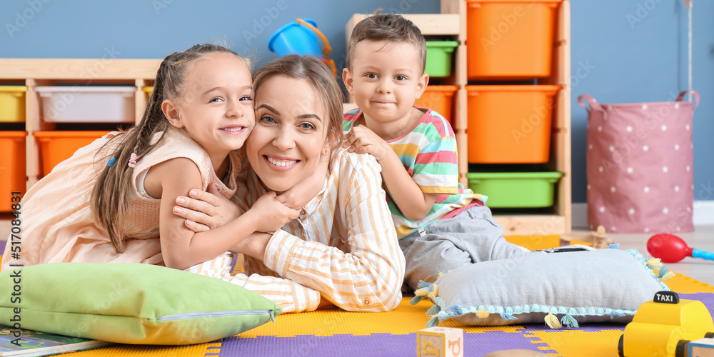 Nanny and cute little children in playroom - obrazy, fototapety, plakaty 