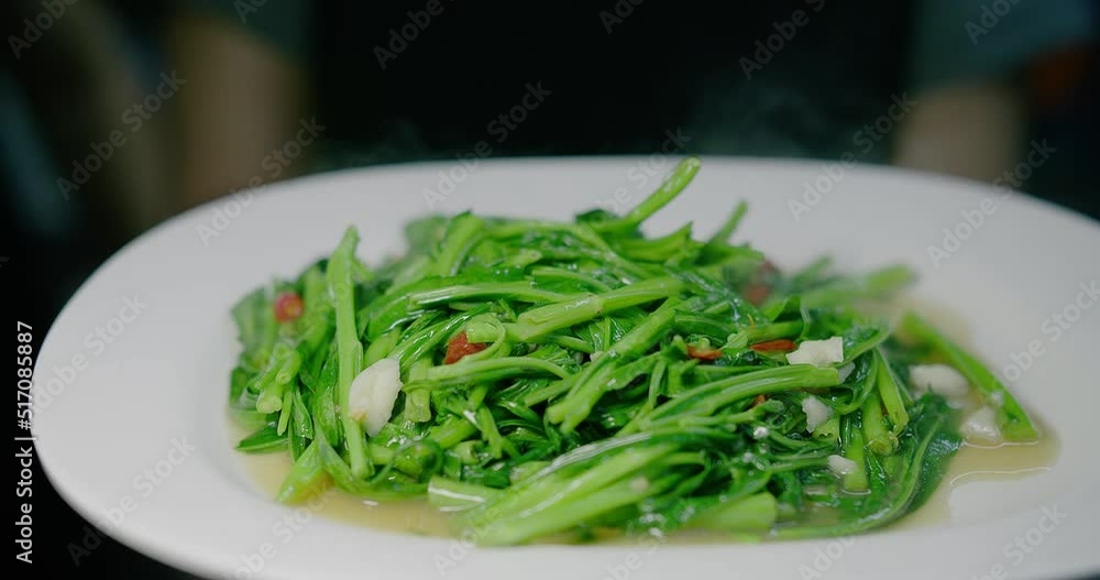 Close up person holding dish of cooked healthy vegetable stir fried fresh green Spicy water spinach seasoned with spicy chili and soy sauce , Thai food, fresh morning glory with red chili and garlic Close up person holding dish of cooked healthy vegetable stir fried fresh green Spicy water spinach seasoned with spicy chili and soy sauce , Thai food, fresh morning glory with red chili and garlic
