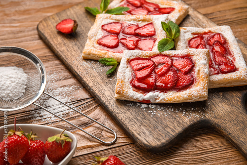 Delicious strawberry puff pastry and sieve with sugar powder on wooden table, closeup