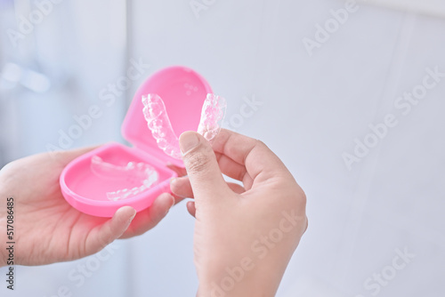 Woman's hand holding an invisible orthodontics made of silicone to put it inside its pink protective cover. Device for teeth alignment. Oral health. photo