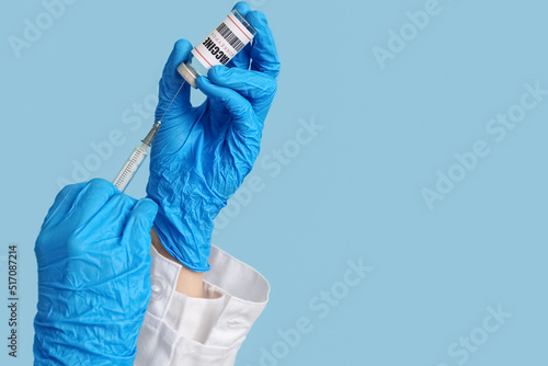 Hands of doctor with monkeypox vaccine and syringe on blue background