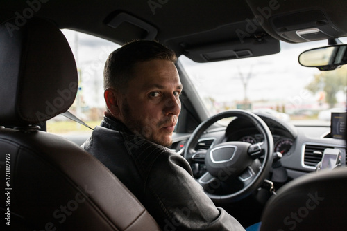 A man looks from behind the wheel of the car to the back of the car in astonishment. Front view.