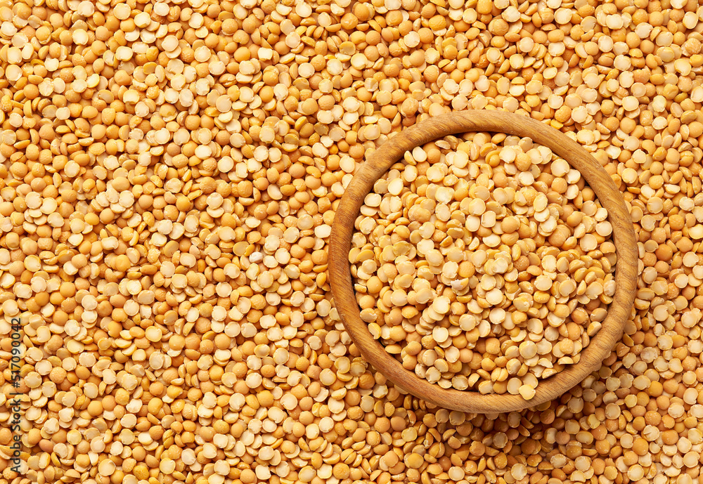 Fototapeta premium wooden plate with dried peas on a yellow peas background close-up top view.