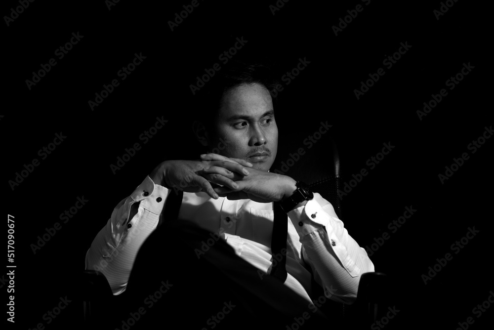 Asian Mafia boss sitting in a chair with a black background.