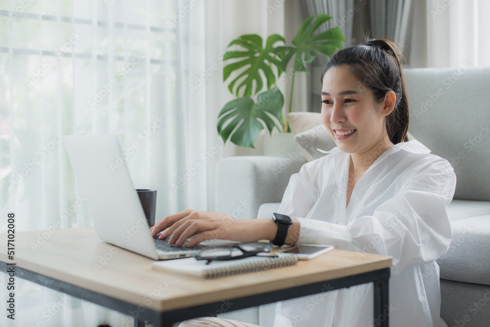 Smiling asian woman relax and sitting on sofa in living room using laptop for work, meeting. Happy young female use laptop talk on applications on gadget and Technology.. Smiling asian woman relax and sitting on sofa in living room using laptop for work, meeting. Happy young female use laptop talk on applications on gadget and Technology..