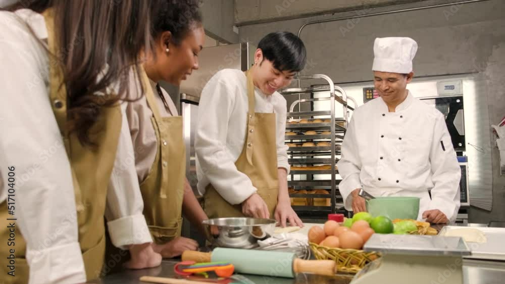 Cuisine course, senior male chef in cook uniform teaches young cooking class students to roll pastry dough before baking, prepare ingredients for bakery foods, fruit pies in stainless steel kitchen. Cuisine course, senior male chef in cook uniform teaches young cooking class students to roll pastry dough before baking, prepare ingredients for bakery foods, fruit pies in stainless steel kitchen.