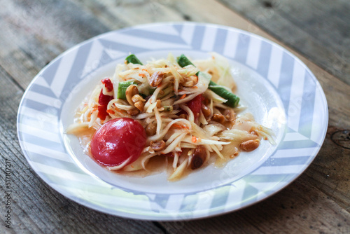 Thai papaya salad on a plate, papaya salad with poop, lemon, pepper, red tomato in white bowl on wooden table