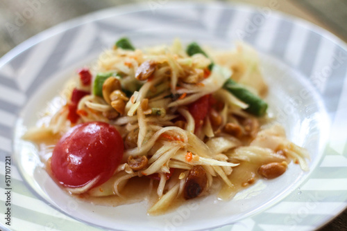 Thai papaya salad on a plate, papaya salad with poop, lemon, pepper, red tomato in white bowl on wooden table