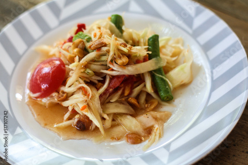 Thai papaya salad on a plate, papaya salad with poop, lemon, pepper, red tomato in white bowl on wooden table