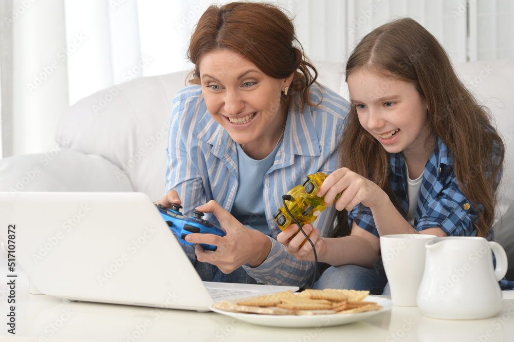 Portrait of smiling mother and daughter using laptop playing video game Portrait of smiling mother and daughter using laptop playing video game