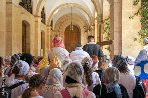 Back view of Orthodox Christian women pilgrims from Europe and  a father carries a crucifix walks the path Jesus carried his cross on the day of his crucifixion on the Via Dolorosa, Jerusalem, Israel