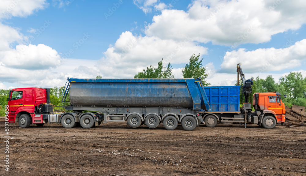 Two trucks are parked at loading dock. Hydraulic manipulator starts loading machines with scrap metal. Two trucks are parked at loading dock. Hydraulic manipulator starts loading machines with scrap metal.