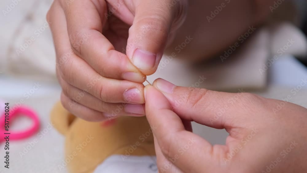 Hand of a seamstress threading a needle, close up. Mother sews a beautiful dress for her little daughter by hand. Hand of a seamstress threading a needle, close up. Mother sews a beautiful dress for her little daughter by hand.