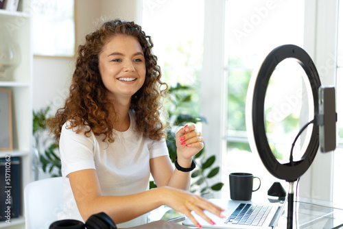 Young curly female blogger recording video at table at home