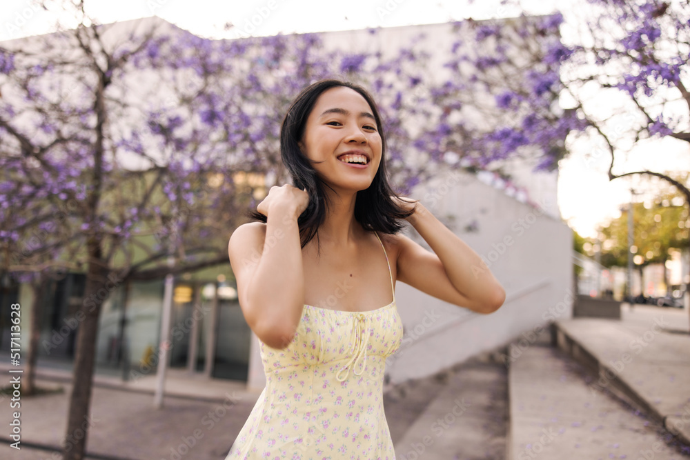 Image of attractive young asian woman walking on the park and smiling . Fair-skinned brunette looking away touching her hair. City style concept Image of attractive young asian woman walking on the park and smiling . Fair-skinned brunette looking away touching her hair. City style concept
