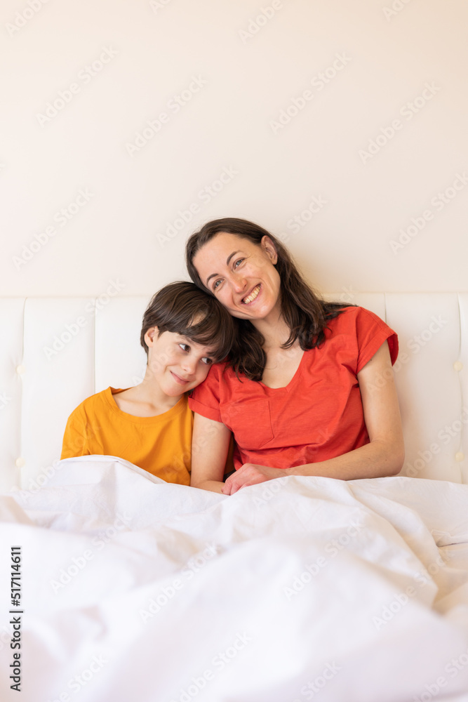 Fototapeta premium A child with mom sit on the bed, a woman hugs her son